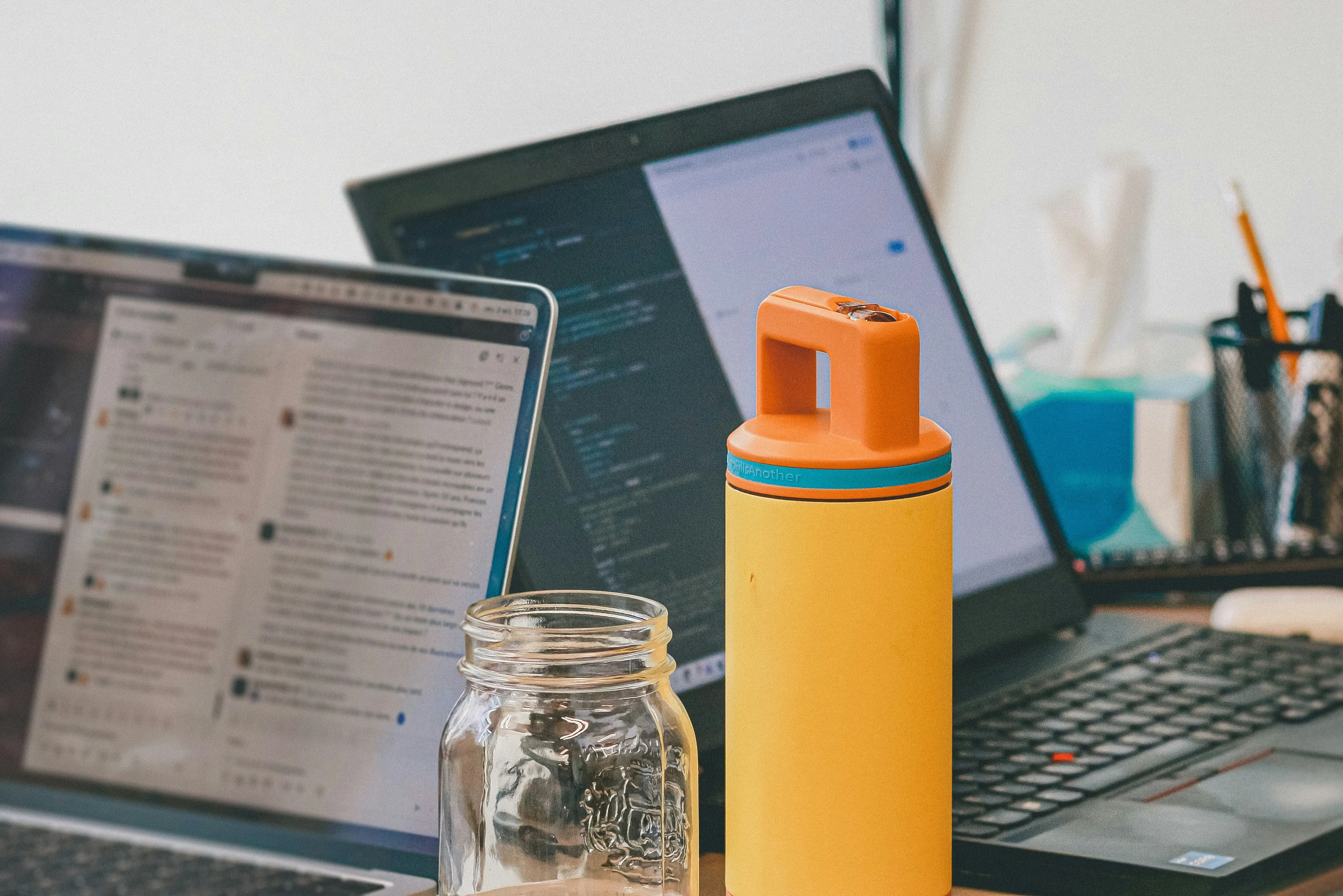 Büroarbeitsplatz mit Laptops, Trinkflasche und Glasgefäß